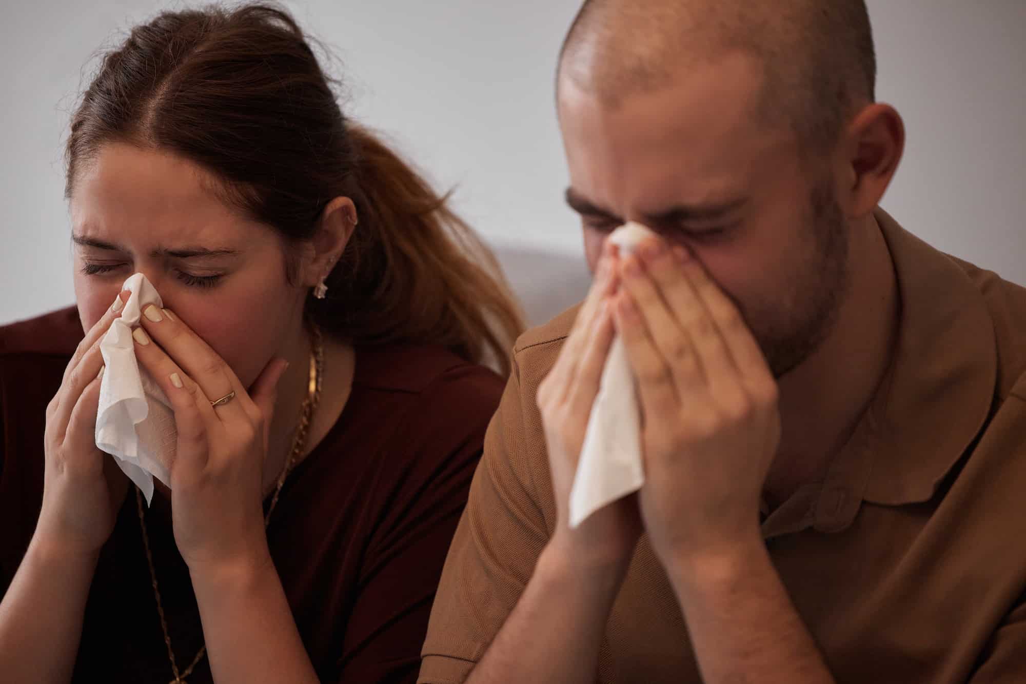 At least were sick together. Shot of a young couple blowing their noses during a cold.