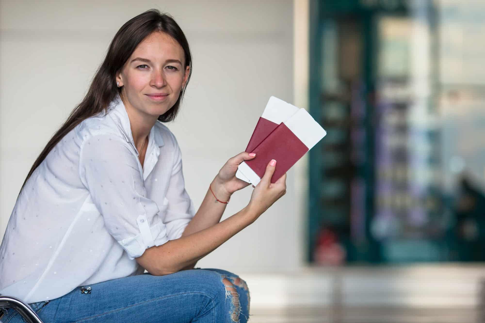 Happy young woman with air ticket and passports at airport waiting for flight