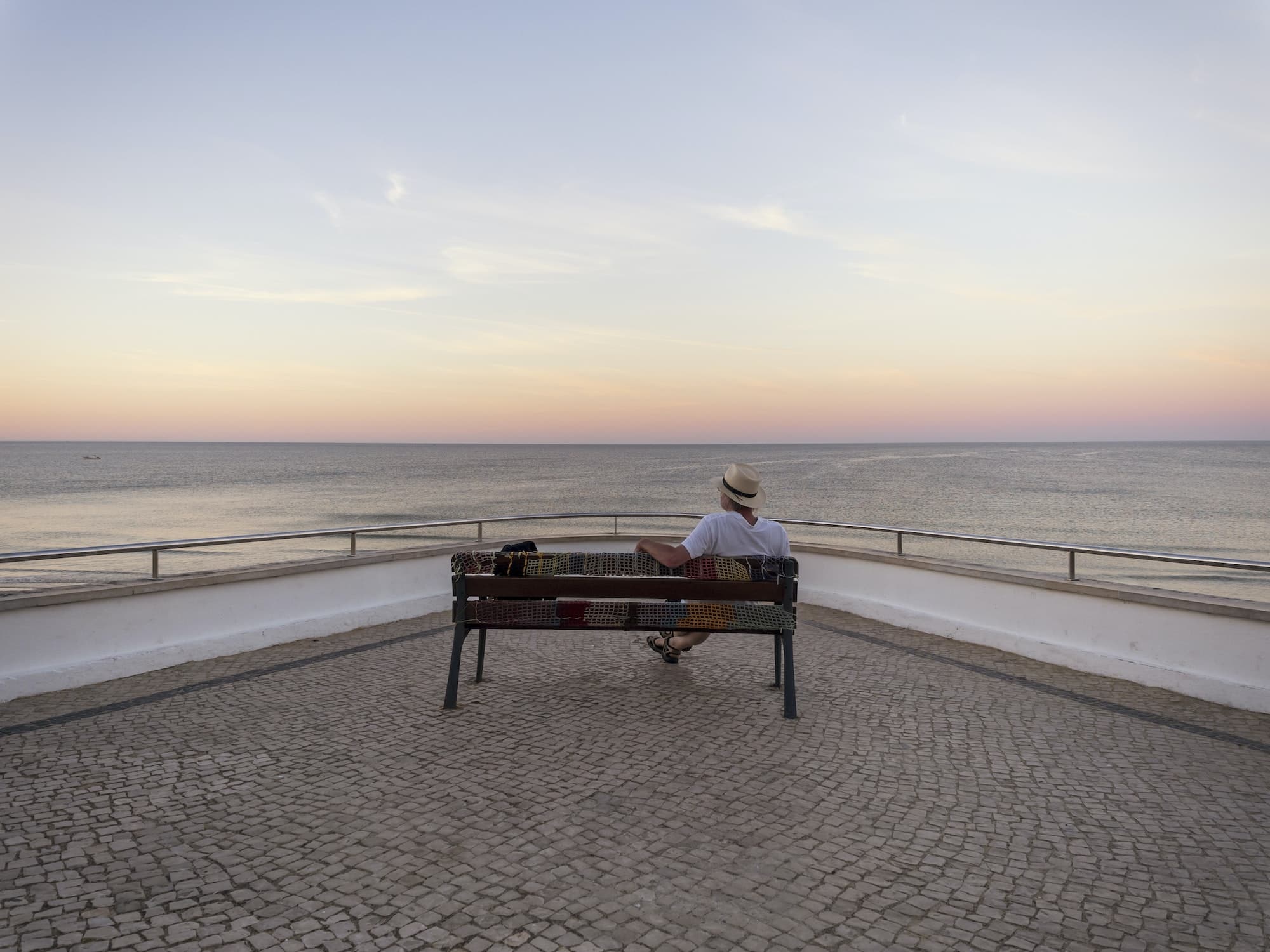 Portugal, Senior man siting on bench watching sunrise