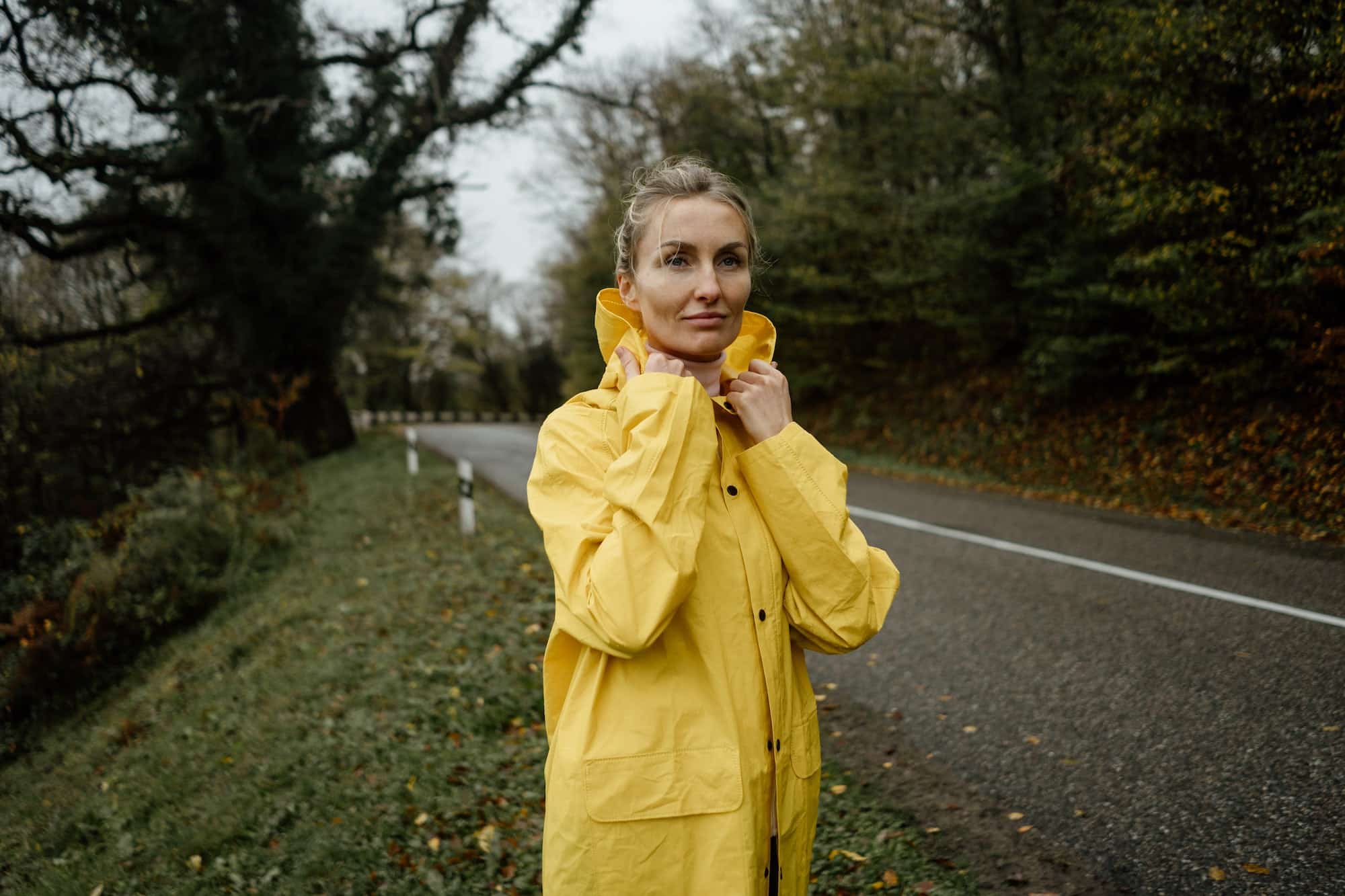 Pretty woman in yellow raincoat walking in rainy weather in the countryside