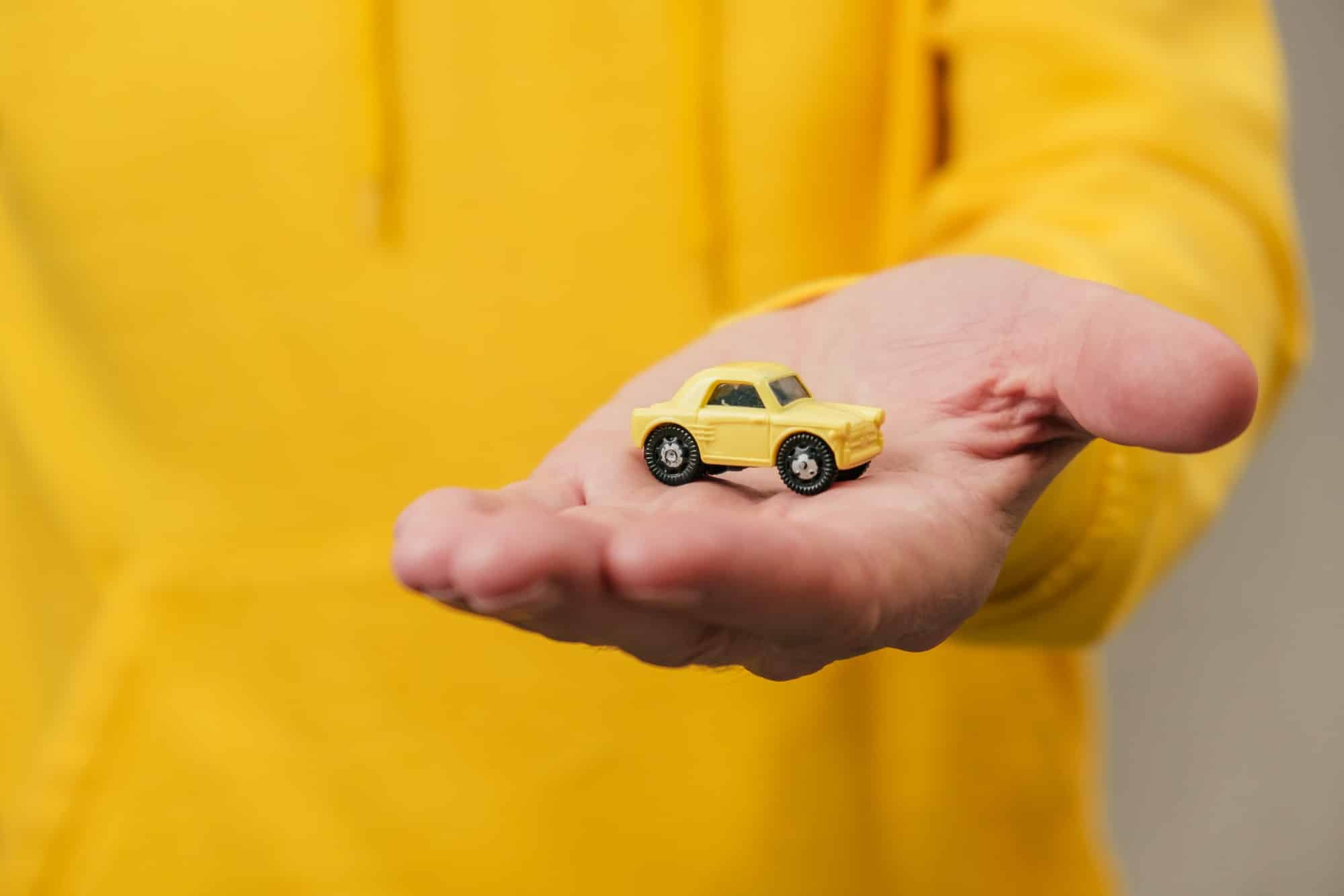 A small yellow toy car in a man's hand. The concept of insurance and protection. Close-up.