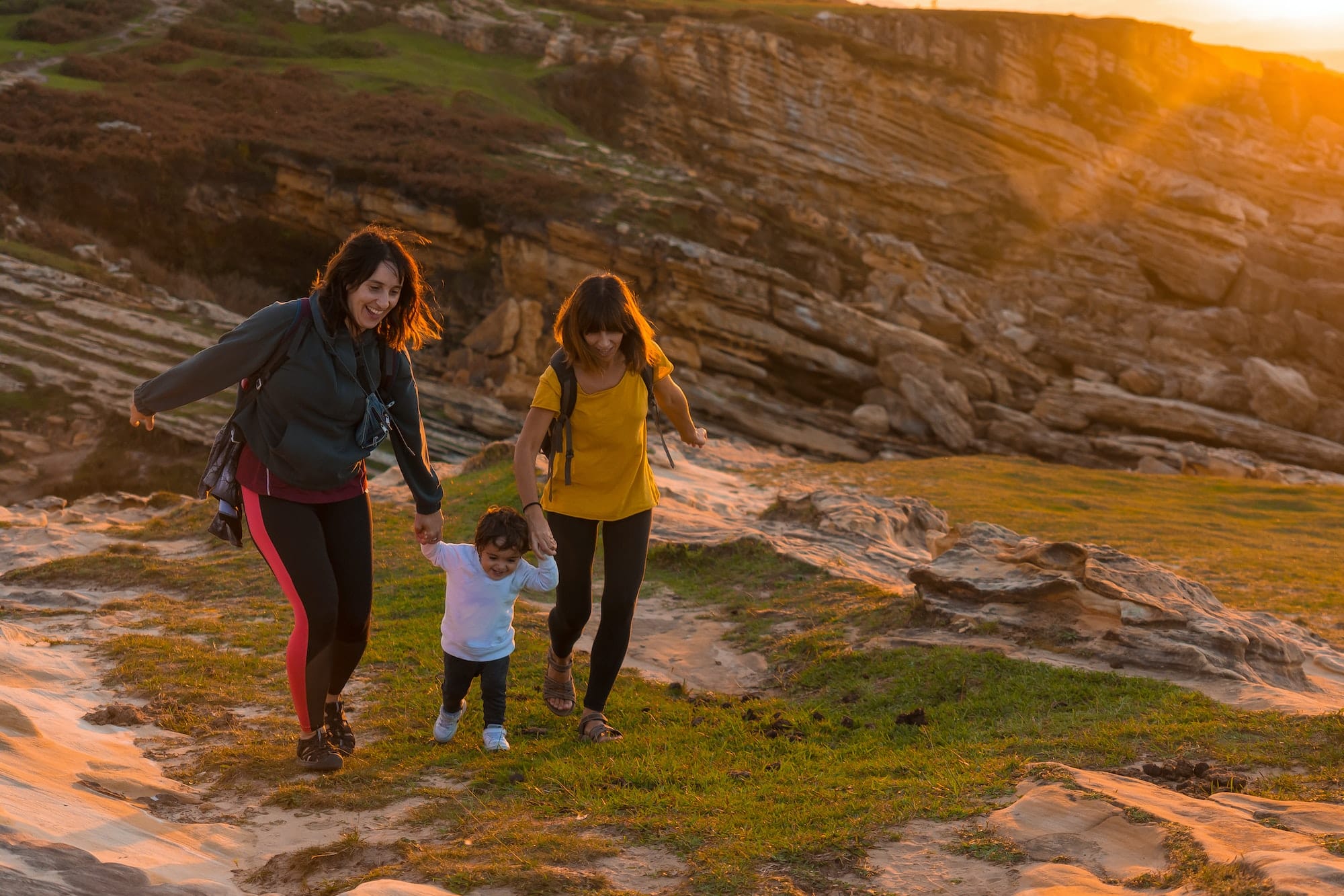 Two sisters with a child watching the sunset on the coast by the sea, family lifestyle