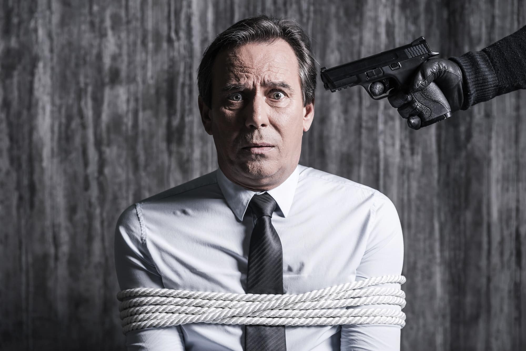 Please no! Tied up businessman caught by a criminal aiming his head with gun