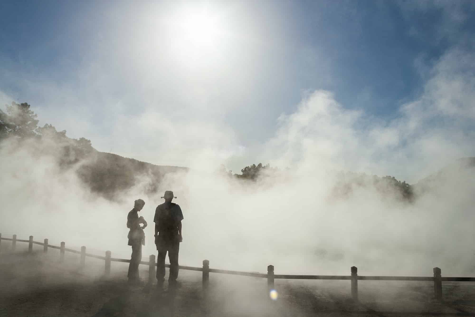 Two people in rising mist at a thermal pool site