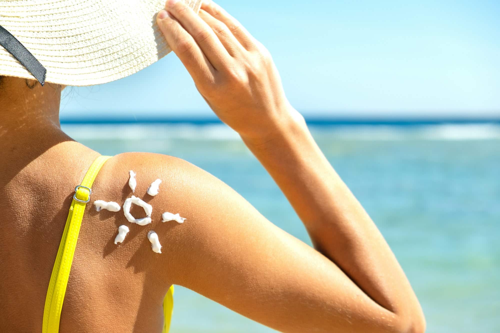 Back view of young woman tanning at the beach with sunscreen cream in sun shape on her shoulder. UV