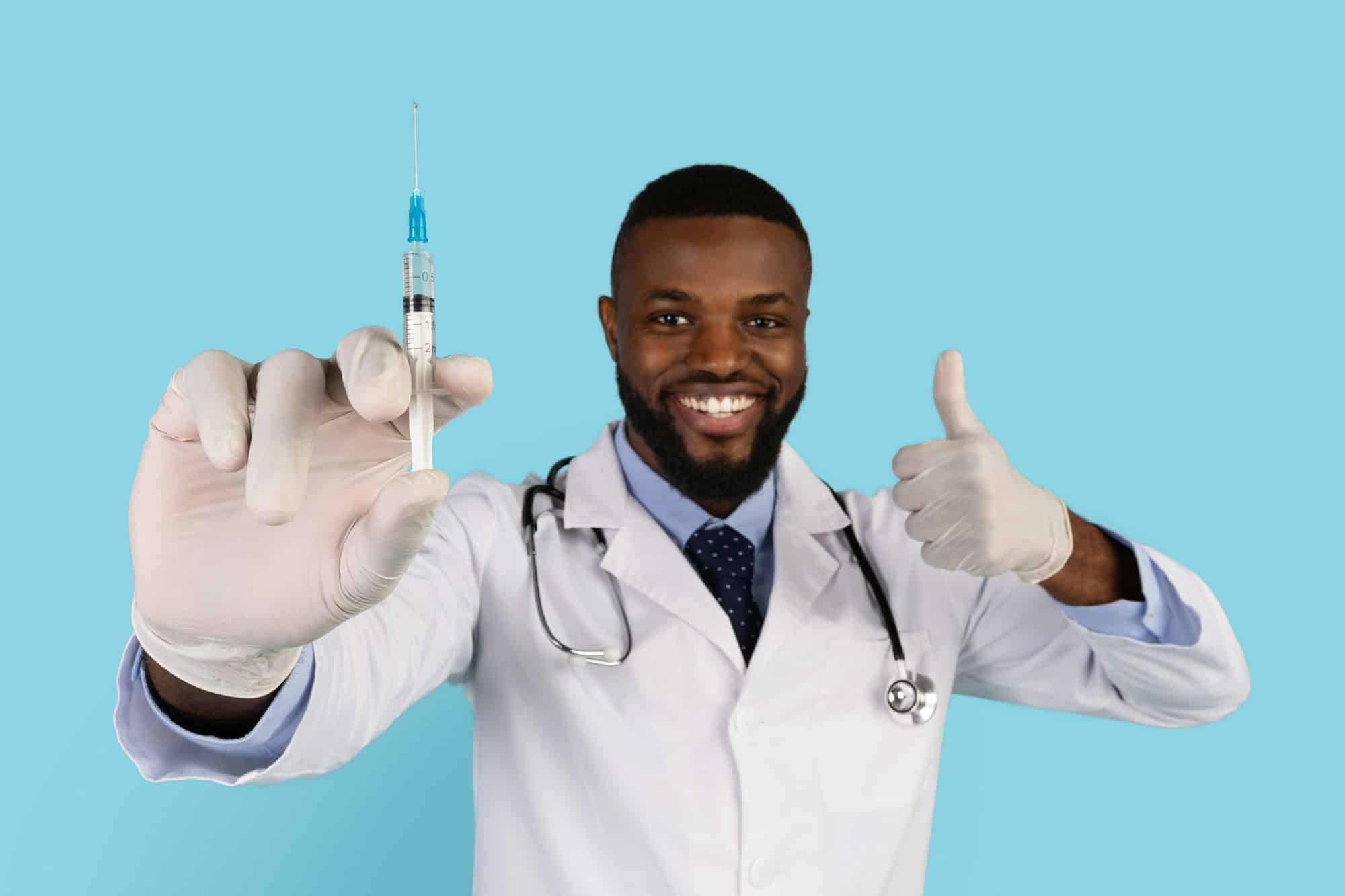 Vacination Campaign. Portrait Of Smiling Handsome Black Doctor With Syringe In Hand