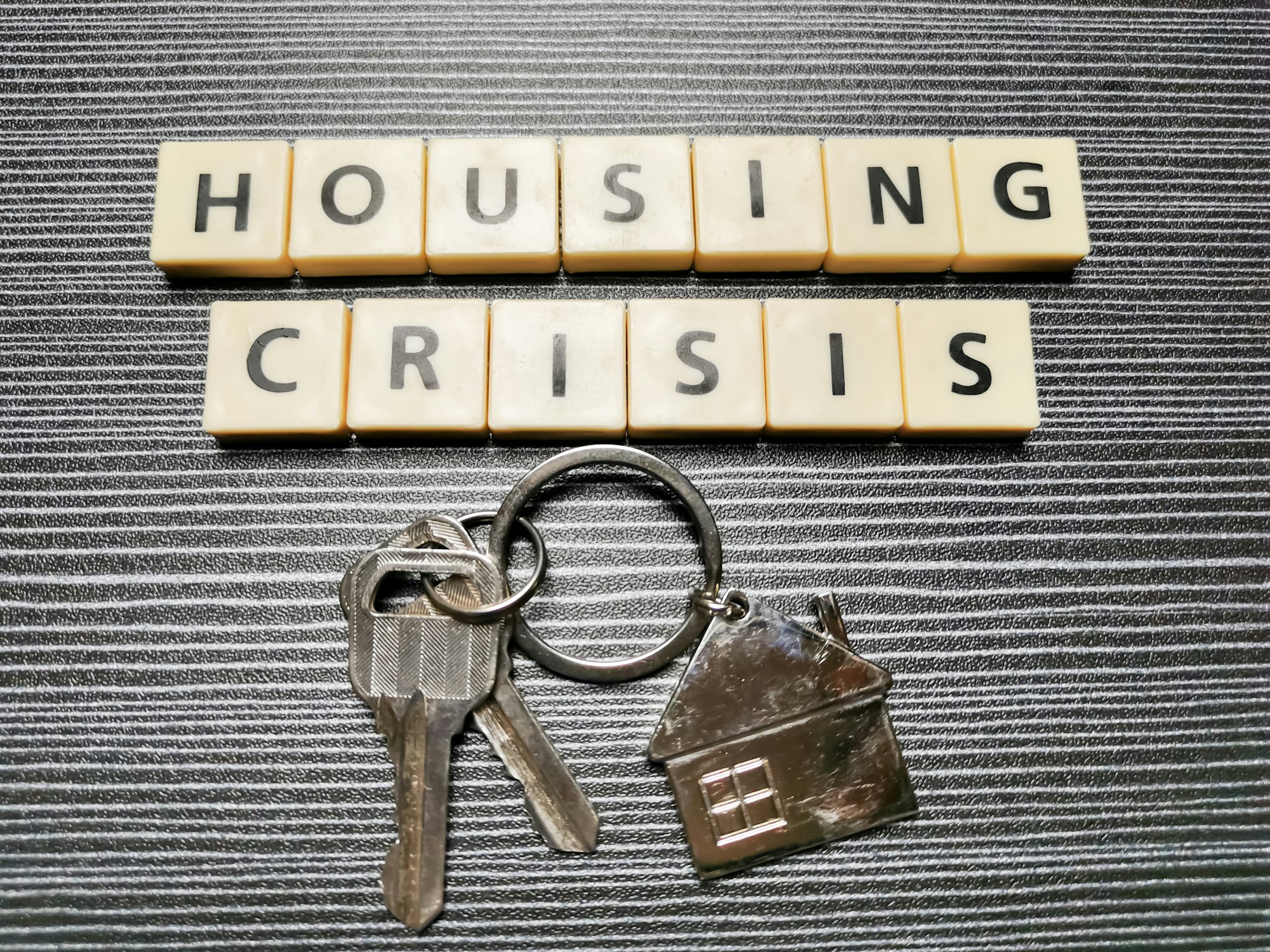 Word housing crisis made from square letter tiles against black background.