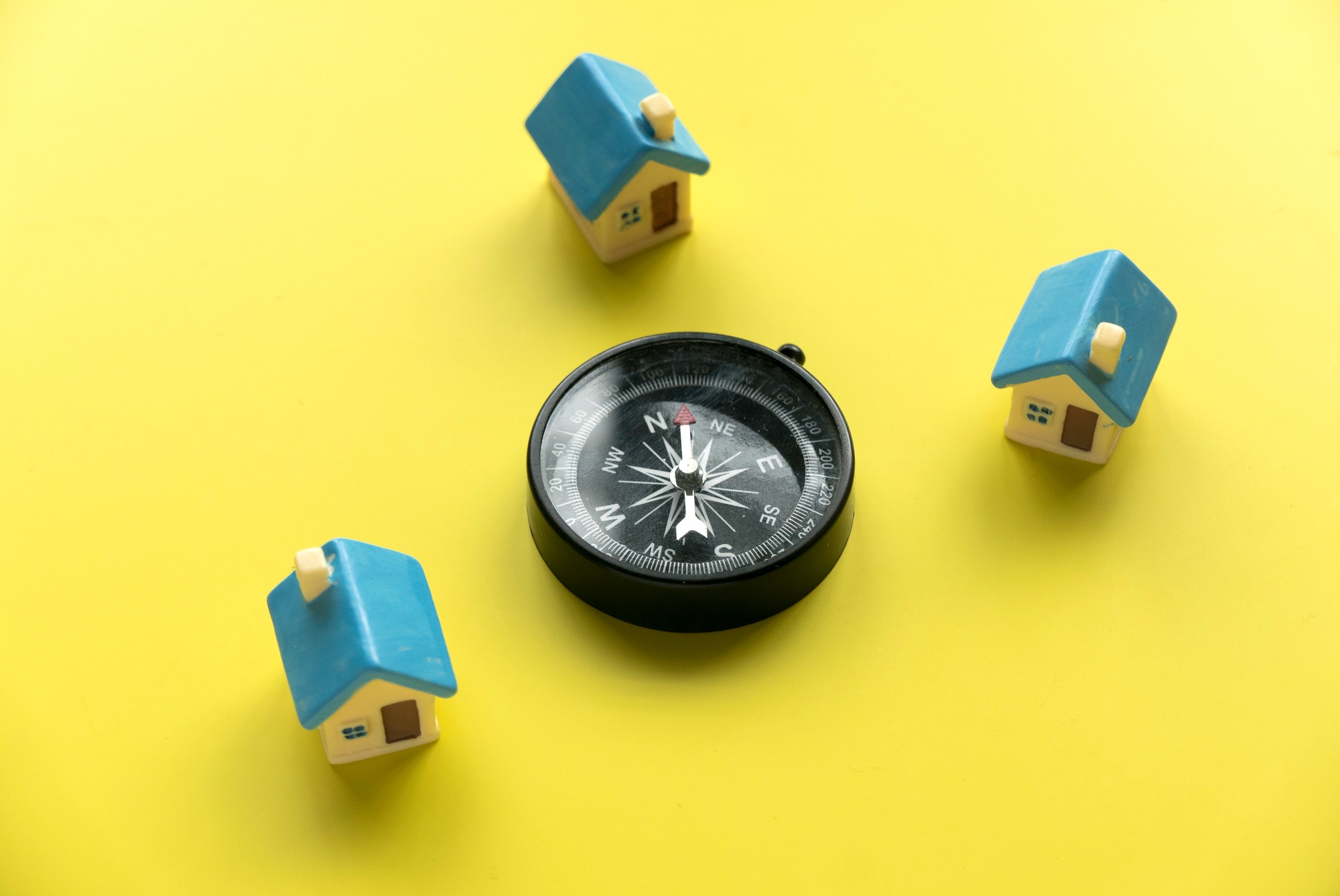 Miniature house and a compass over a yellow background.