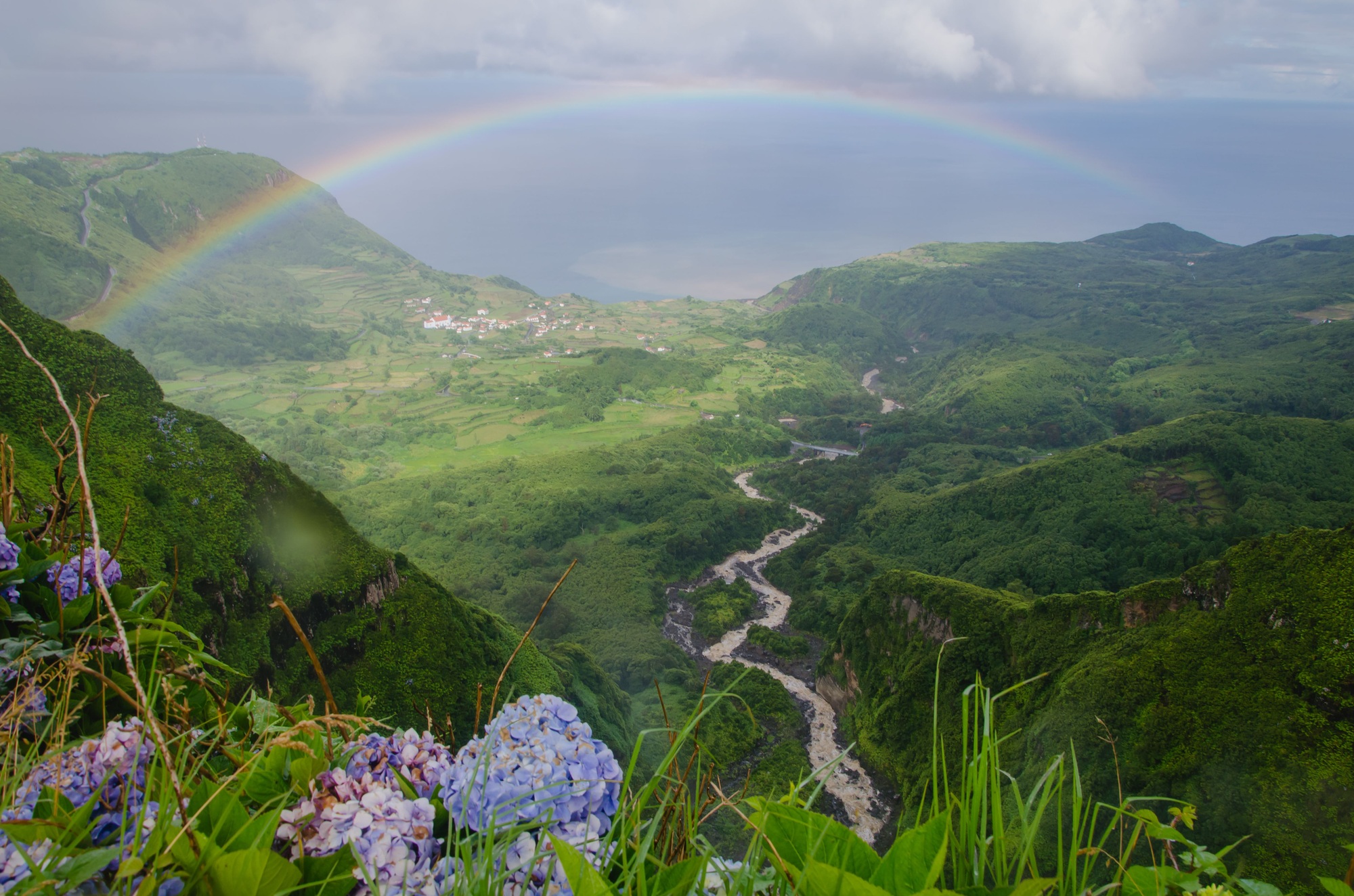 Rainbow arch over the mountains covered with greenery in Flores Island